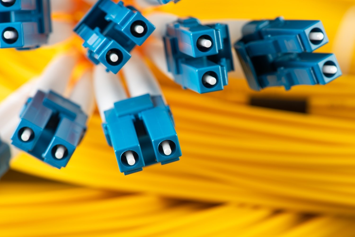 Blue fiber connectors in front of coils of yellow fiber optic cables