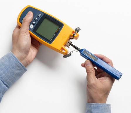 The connector port of a yellow handheld Fluke tester being cleaned with a Quick Clean tool