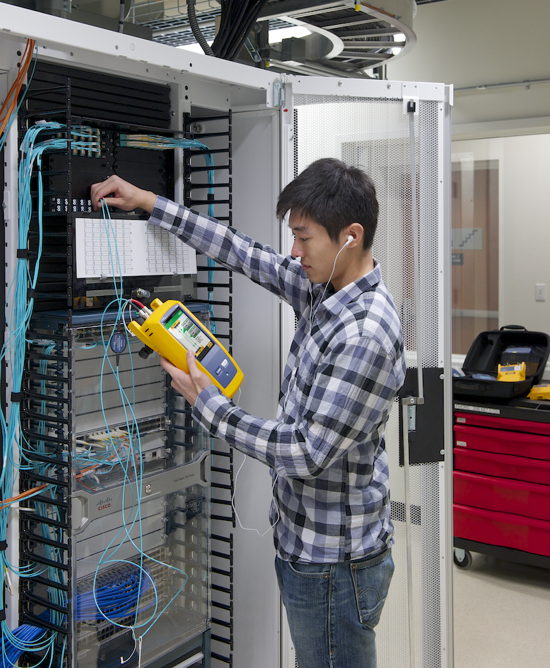 Man in front of a rack testing fiber optic cabling