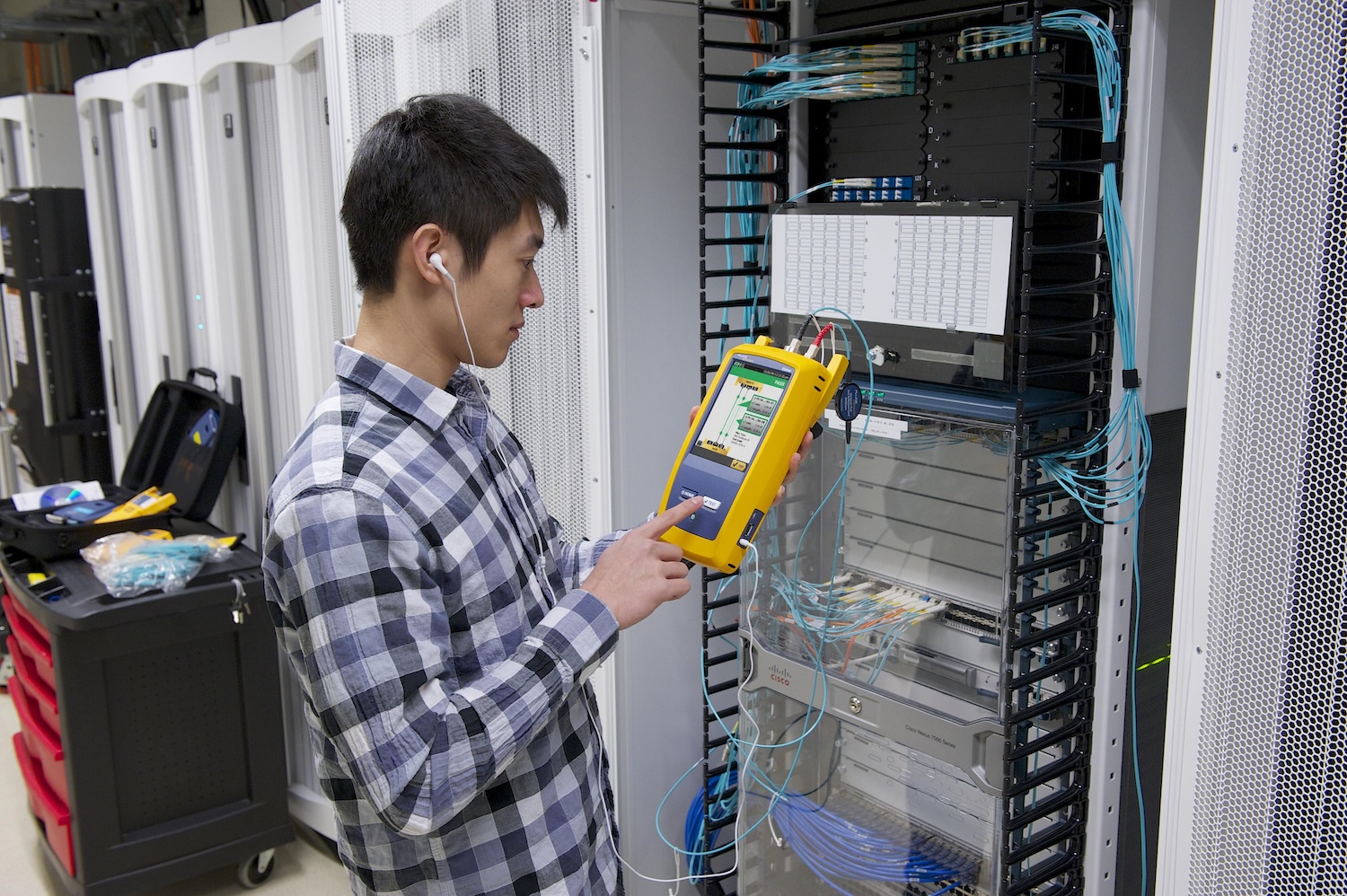 Man standing in front of an equipment rack, using a Fluke Networks Versiv tool