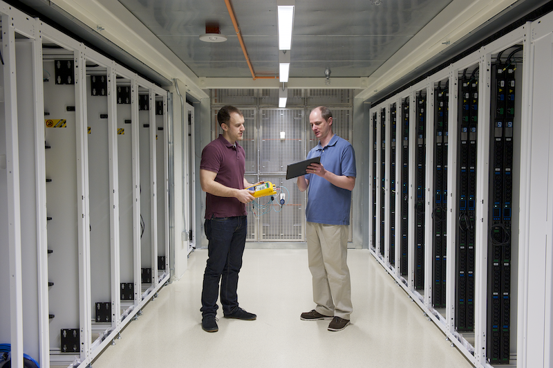 Two men conferring with each other in a data center aisle during installation