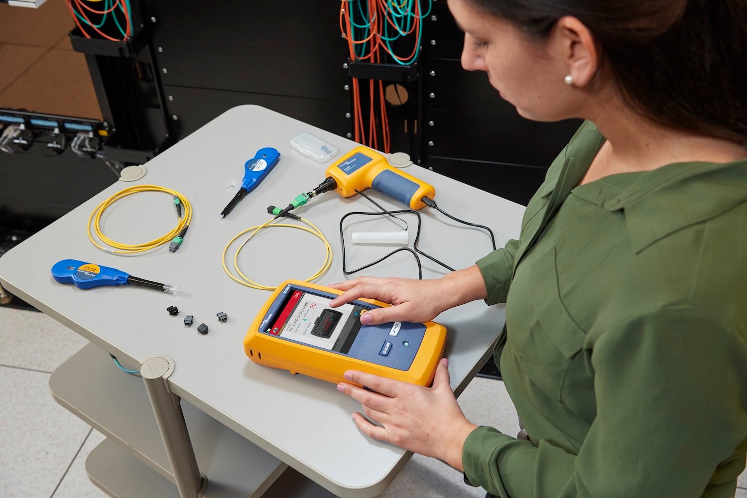 Woman in green shirt using an FI-3000 FiberInspector Pro to inspect a recently cleaned fiber cable lying on a gray tabletop