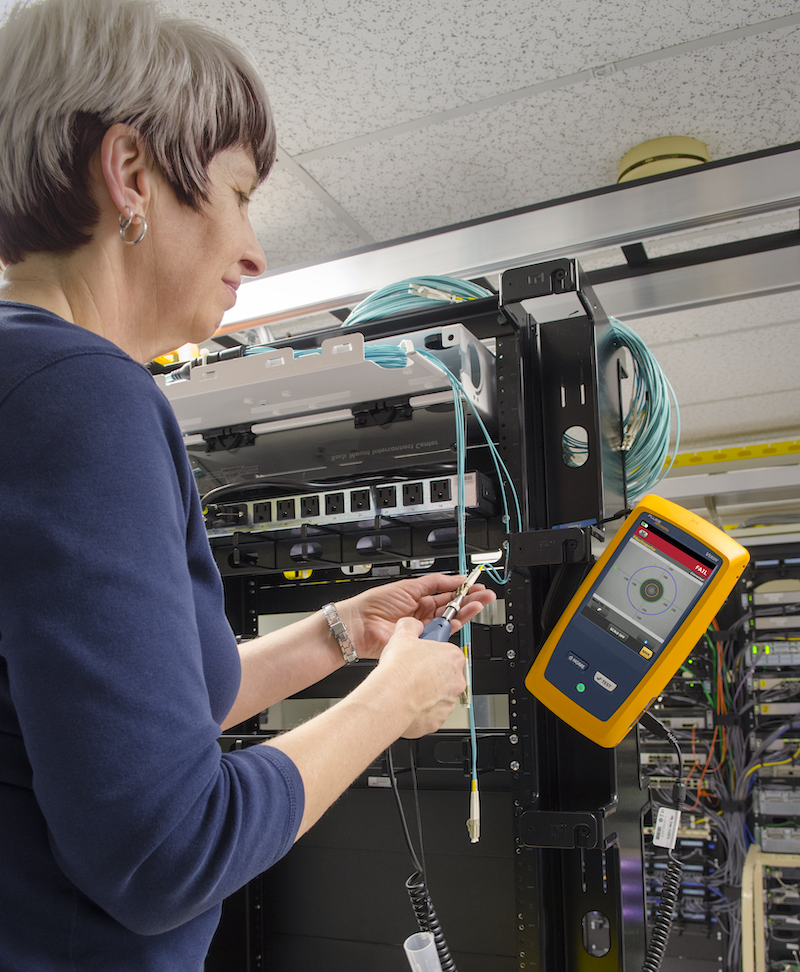 Woman in front of a rack using a fiber inspection tool on fiber optic cabling