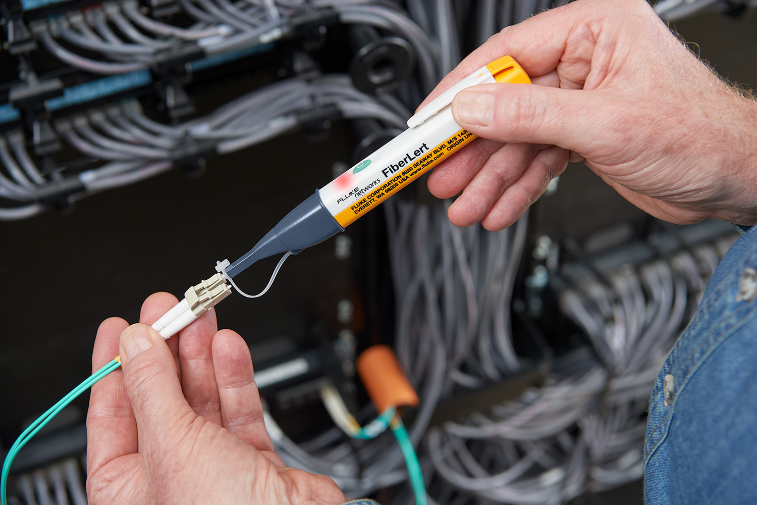 Hands holding a FiberLert tool against the end of a fiber optic cable