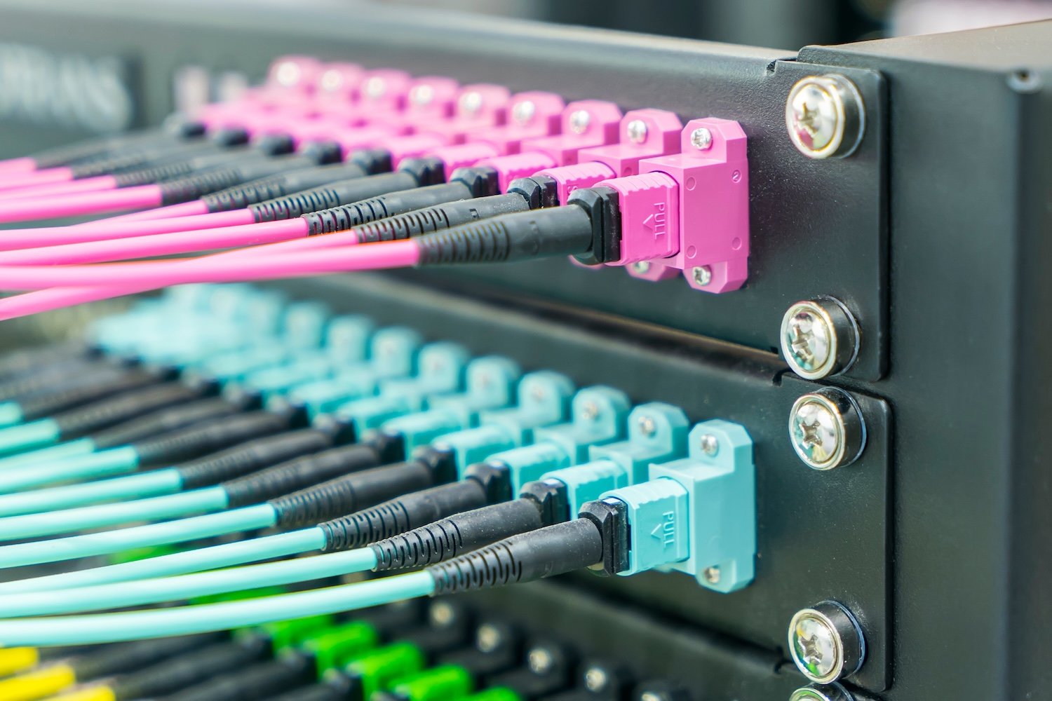 Colorful fiber optic cable connectors plugged into a black patch panel.